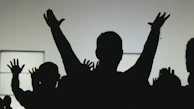 A sunset silhouette of volunteers raising their hands together, symbolizing unity and strength.