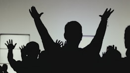 Hands raised in unity silhouetted against a glowing black and orange backdrop.