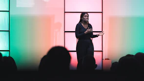 Keynote speaker presenting passionately on stage with a vibrant backdrop