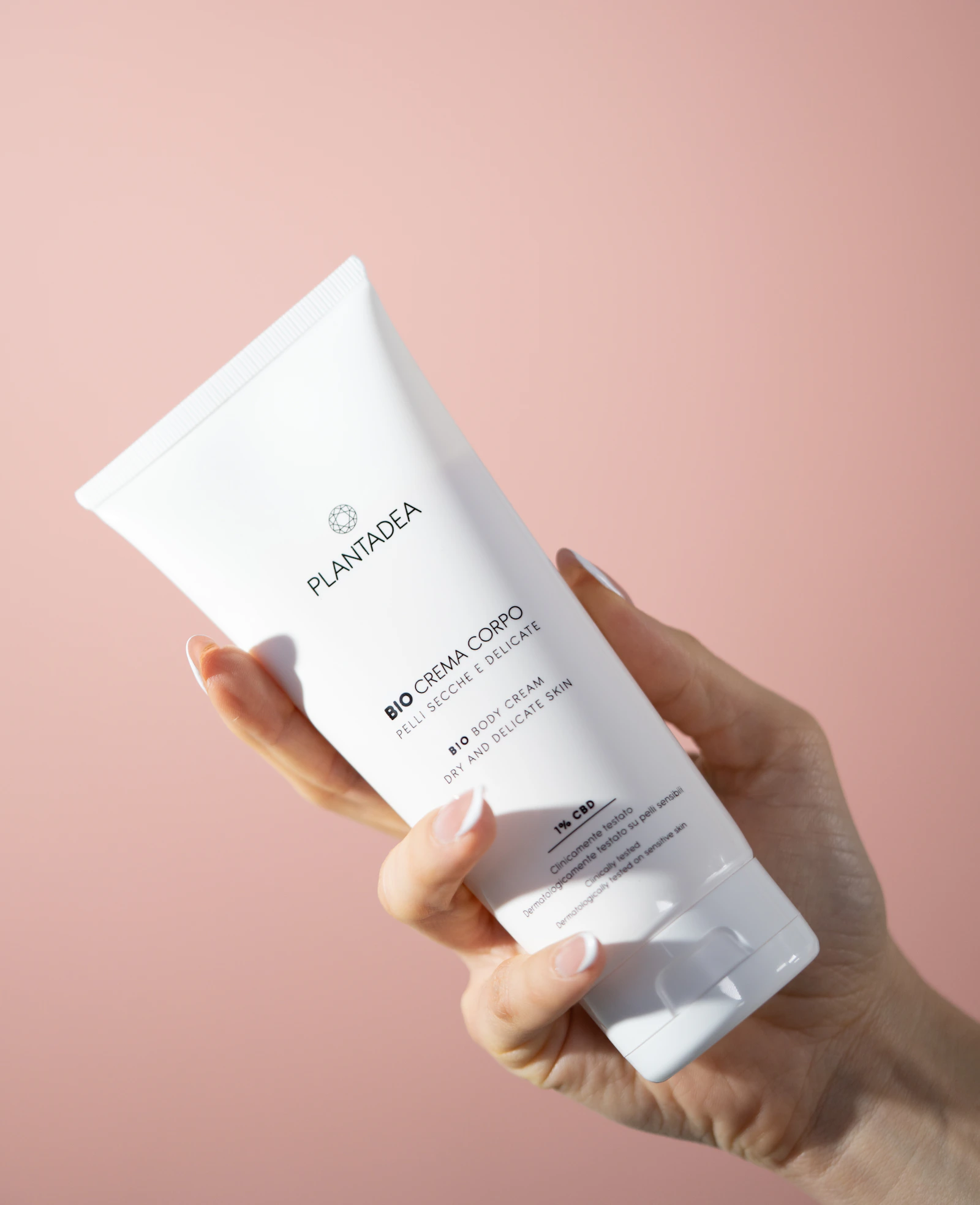 A hand holding a premium body cream tube against a soft neutral background