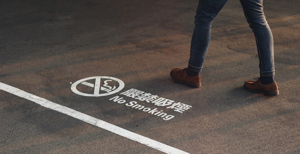 a man walking across a street next to a no smoking sign