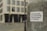 A sticker with German text 'Demokratie, Grundrechte, Rechtsstaat & Freiheit' is attached to a weathered metallic surface, likely a pole. The background features a blurred view of a city street and a modern building with multiple windows.