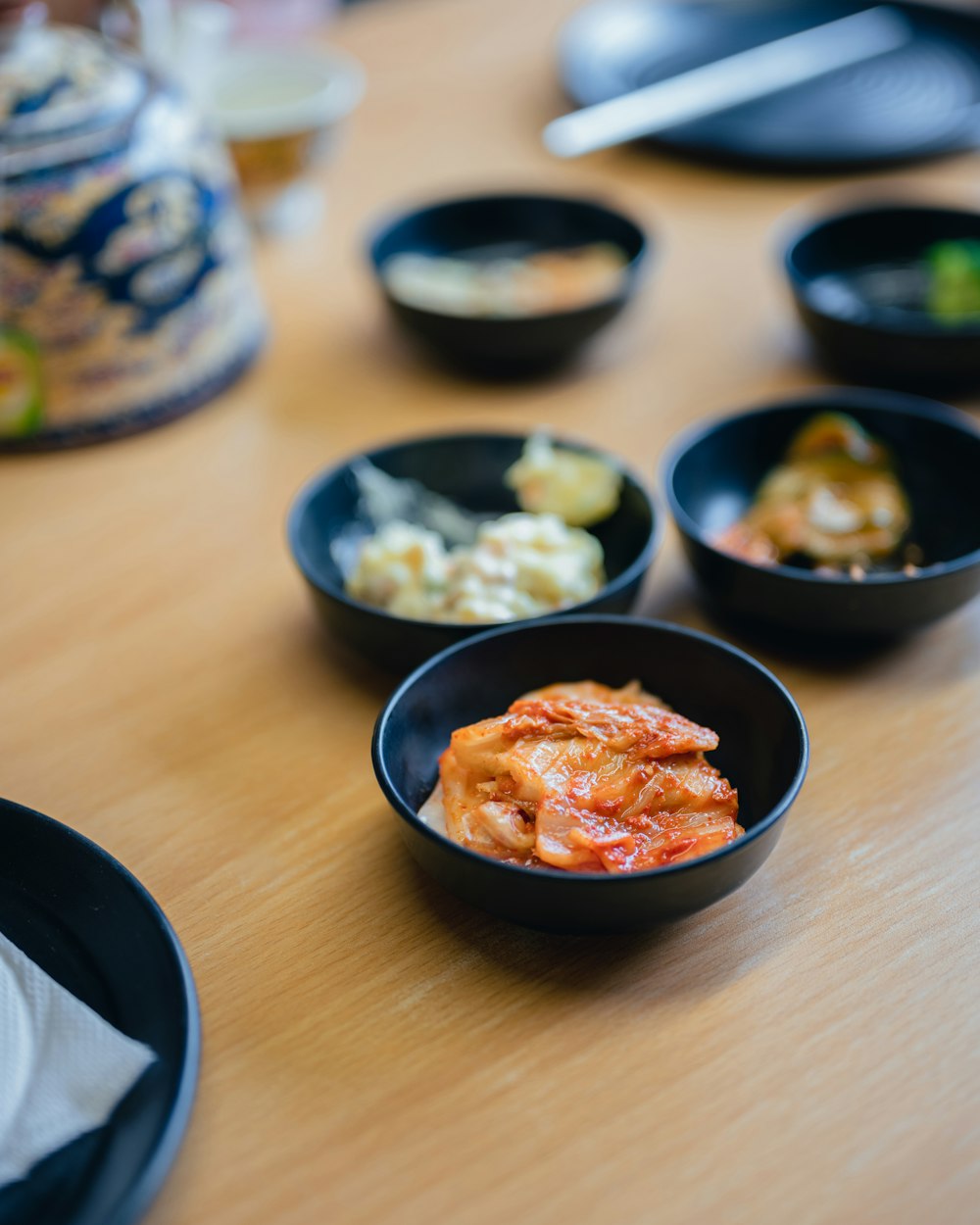 a wooden table topped with black bowls filled with food