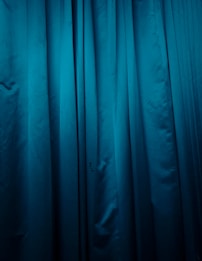 Deep blue fabric with vertical folds and a smooth texture, suggesting it might be a curtain or drapery.