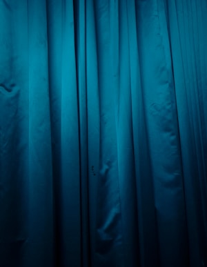 Deep blue fabric with vertical folds and a smooth texture, suggesting it might be a curtain or drapery.