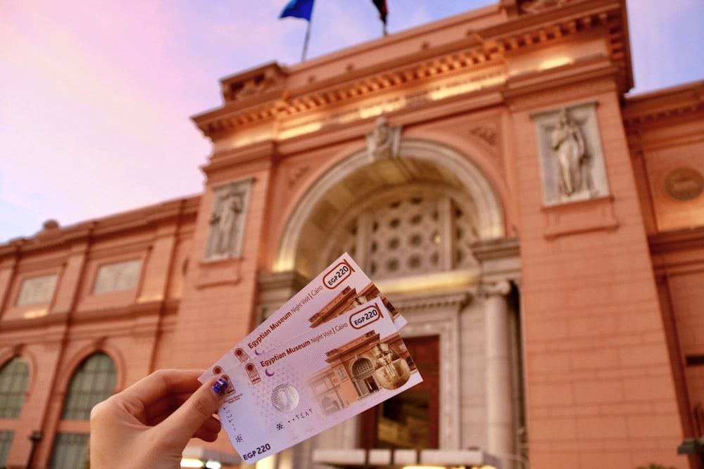 a person holding up two bills in front of a building