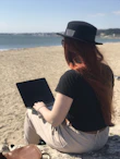 A digital nomad working on a laptop from a beach.