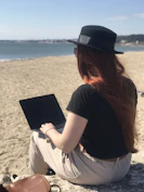 A digital nomad working on a laptop from a beach.