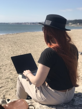 A warm portrait of a confident woman working on her laptop by the beach at sunset.