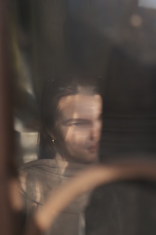An intimate image of a transgender individual looking out a window, soft reflections framing their face.