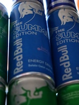Several cans of energy drink with a prominent branding design. The cans feature a blue and green color scheme, with the phrase 'The Summer Edition' highlighted on the label.