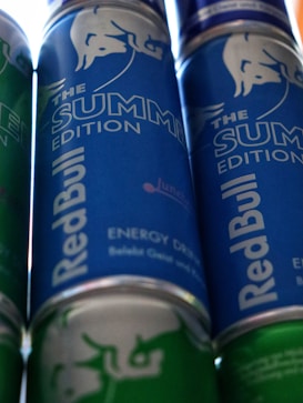 Several cans of energy drink with a prominent branding design. The cans feature a blue and green color scheme, with the phrase 'The Summer Edition' highlighted on the label.