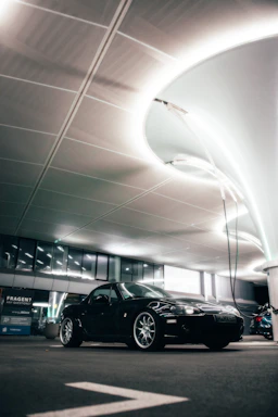 A sleek black sports car under soft white LED lighting in a modern detailing studio