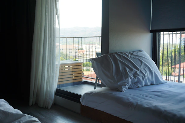 Bright, airy bedroom with minimalist decor and large windows overlooking Kuala Lumpur skyline.