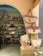 A quaint shop entrance displaying a variety of woven baskets, some hanging and some stacked. Inside, shelves are filled with metallic decorative items and colorful tote bags. The arched entrance features intricate patterns.
