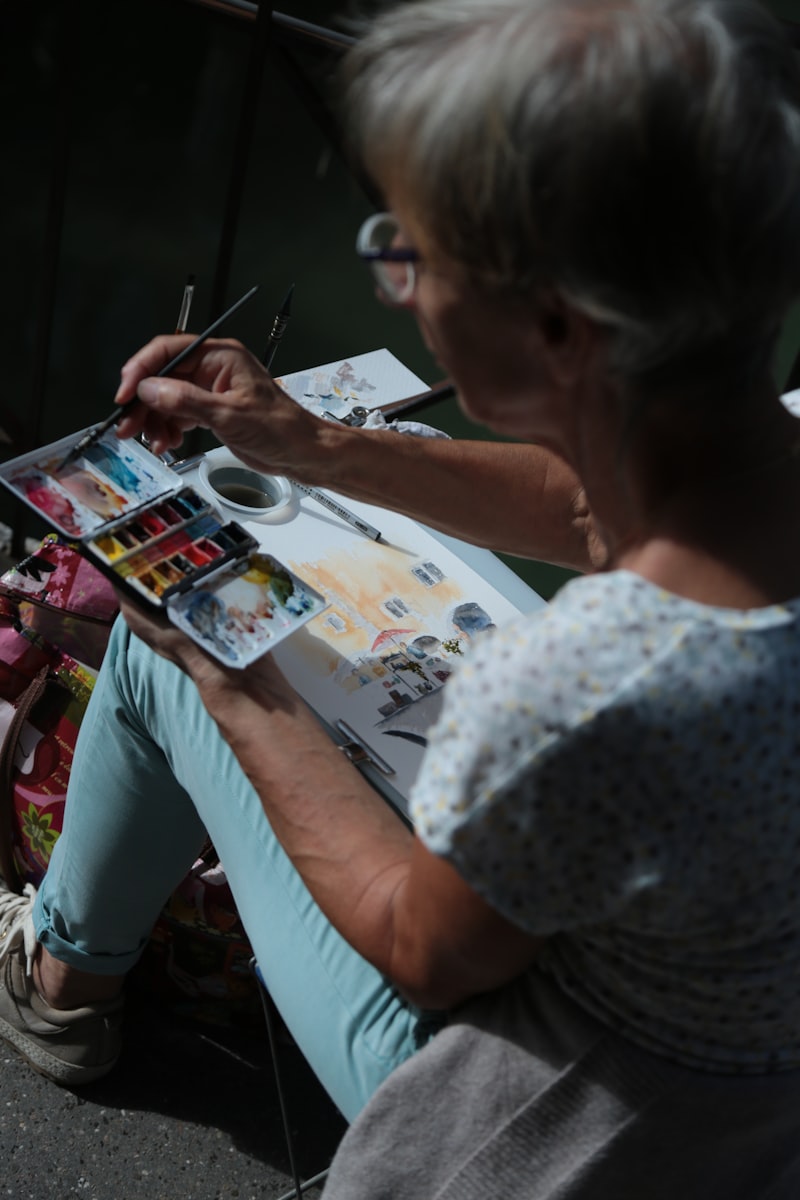 Senior woman watercolor painting outdoors on a sunny day, enjoying a creative hobby after 65
