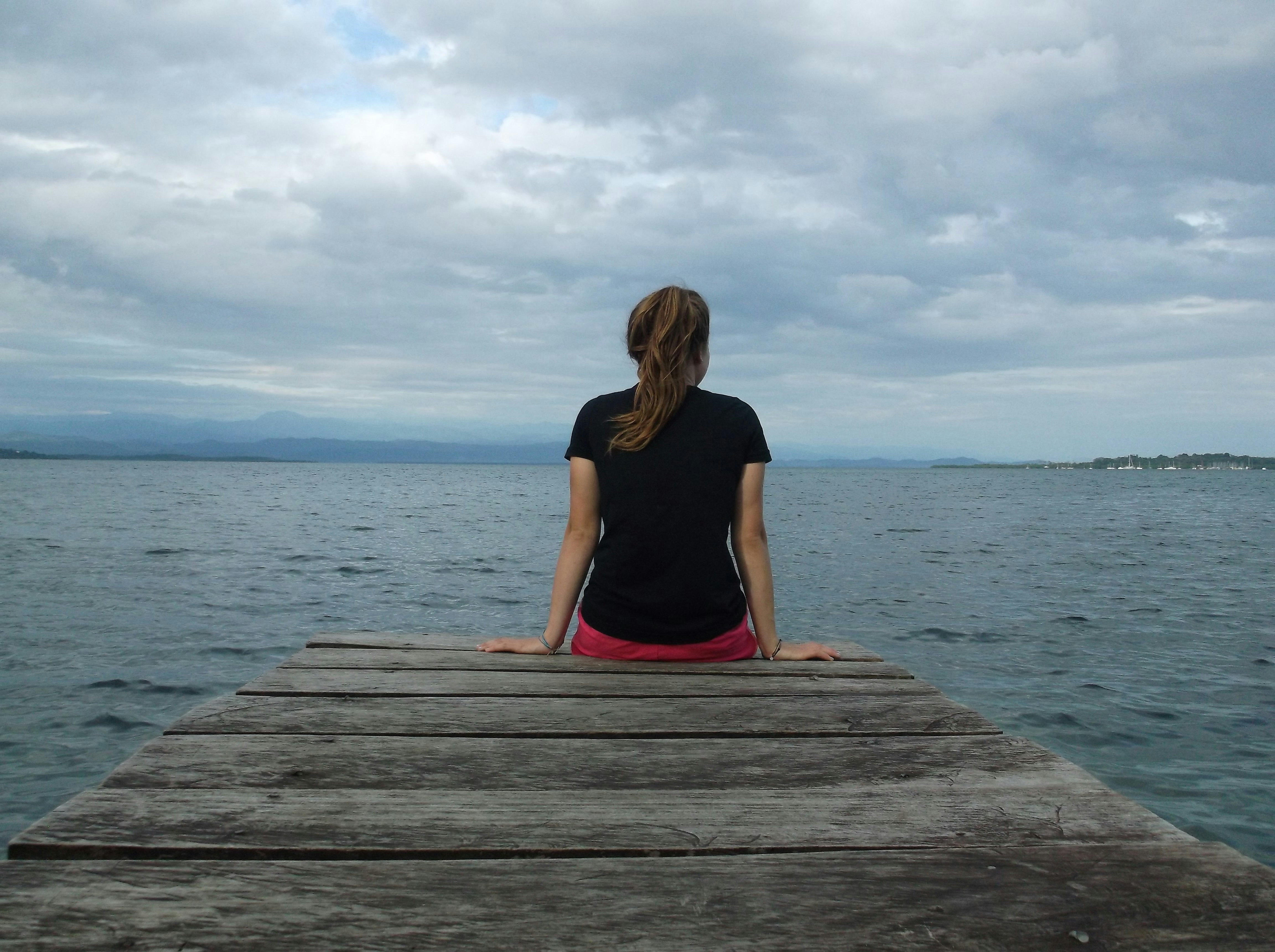 A woman sitting on a dock looking out at the water photo – Free Outward ...