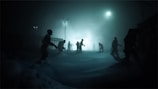 Silhouettes of ominous figures are shrouded in fog under dim streetlights, set in a dark and eerie landscape.