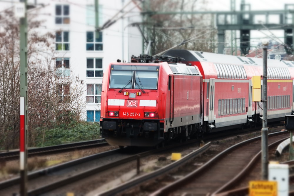 a red train traveling down train tracks next to a tall building