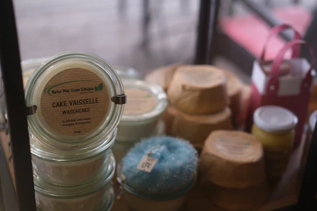 Various jars and recyclable packaging are arranged neatly, featuring a product labeled 'Cake Vaisselle Waschcake'. These are eco-friendly cleaning products displayed on a shelf, with a focus on sustainability and aesthetics. A pink container and a yellow jar are visible among the items.