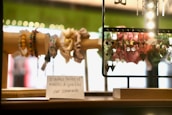 A display of colorful handmade bracelets and dangling earrings is set on a wooden stand. The bracelets are made of various beads, while the earrings are intricate and decorative. There is a small sign in French indicating the availability of different sizes and models.