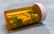 A translucent orange prescription pill bottle lies on its side, containing a mix of yellow and green tablets. The tablets are marked with numbers and letters. The white cap is securely attached, and the background is a soft, blurred blue.