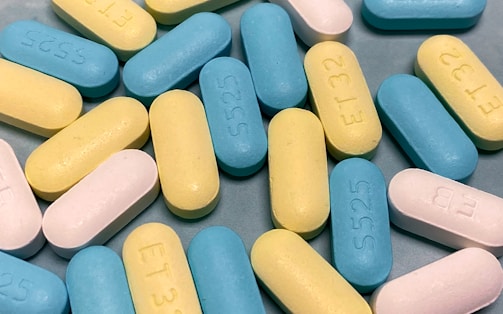 A close-up view of several oval-shaped pills in varied pastel colors, including blue, yellow, and white, scattered on a flat surface.