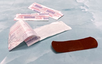 Several adhesive bandage strips are placed on a light blue surface. An open wrapper reveals one brown bandage strip, while other bandages are still wrapped.