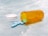 A transparent orange pill bottle lies on its side on a light blue, textured surface. The white cap is off to the side, and several light blue, oval-shaped tablets have spilled out onto the surface.