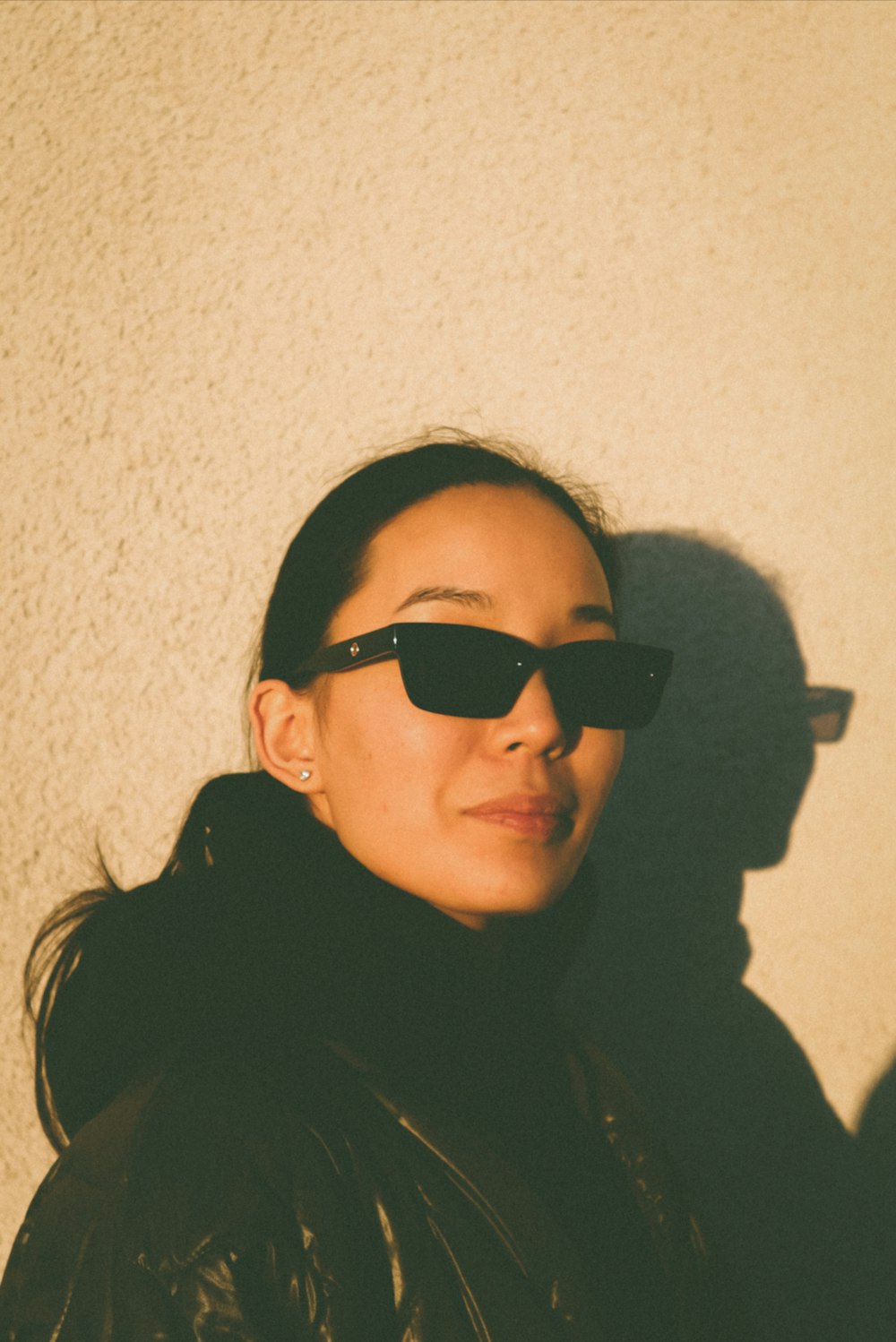 Eine Frau mit Sonnenbrille steht neben einer Wand
