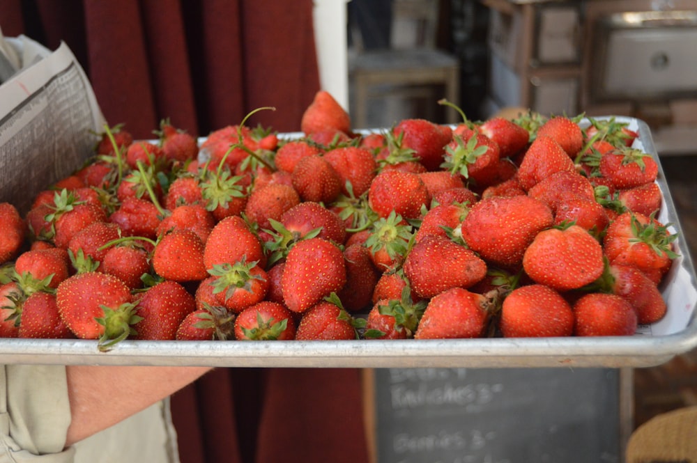 a person holding a tray of strawberries in their hands