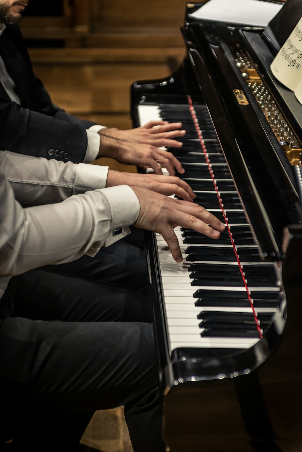 two people sitting at a piano with their hands on the keys