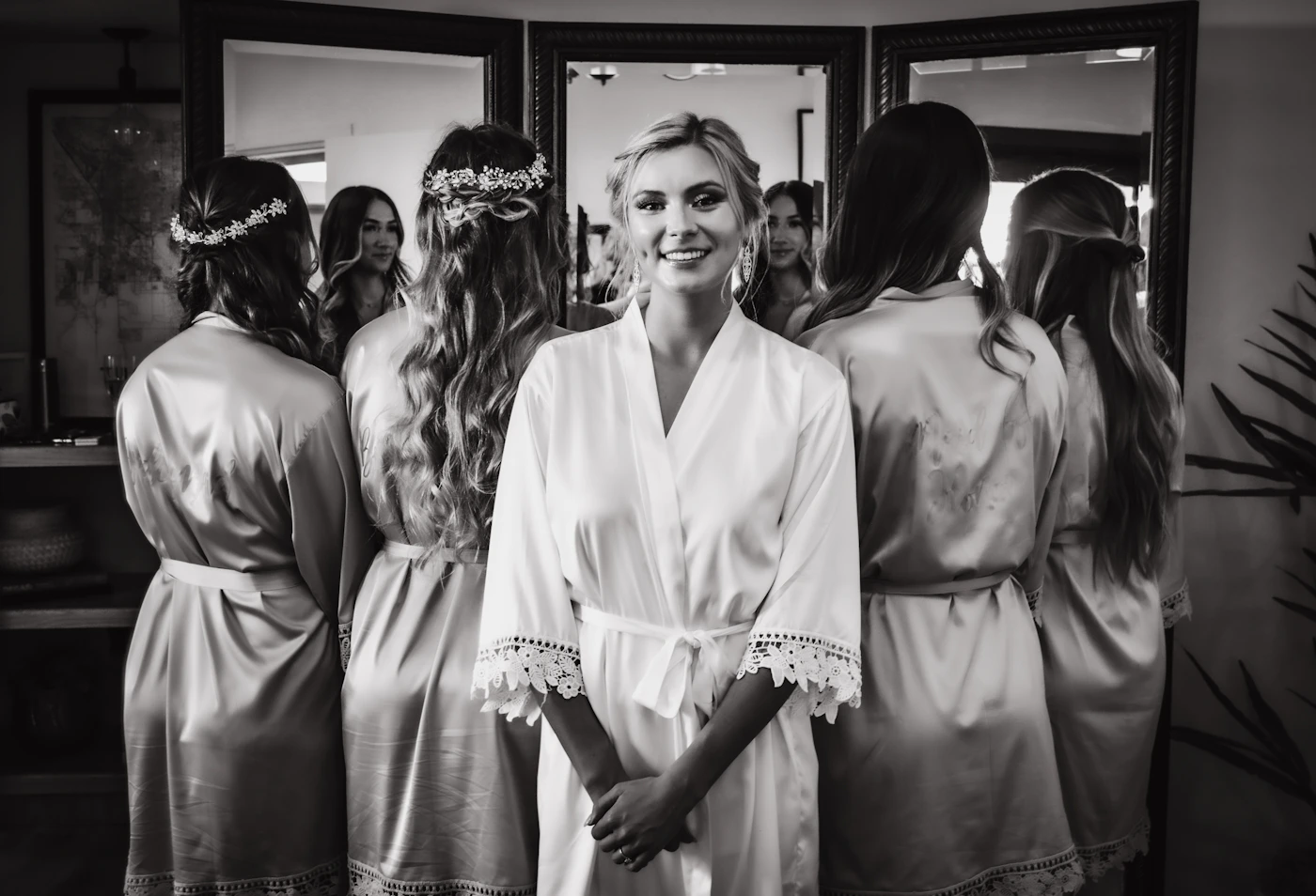Bride in white satin robe standing in front of mirror during wedding morning getting ready preparations