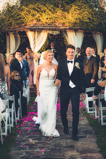 A joyful bride and groom smiling as they walk through a beautifully decorated garden aisle.