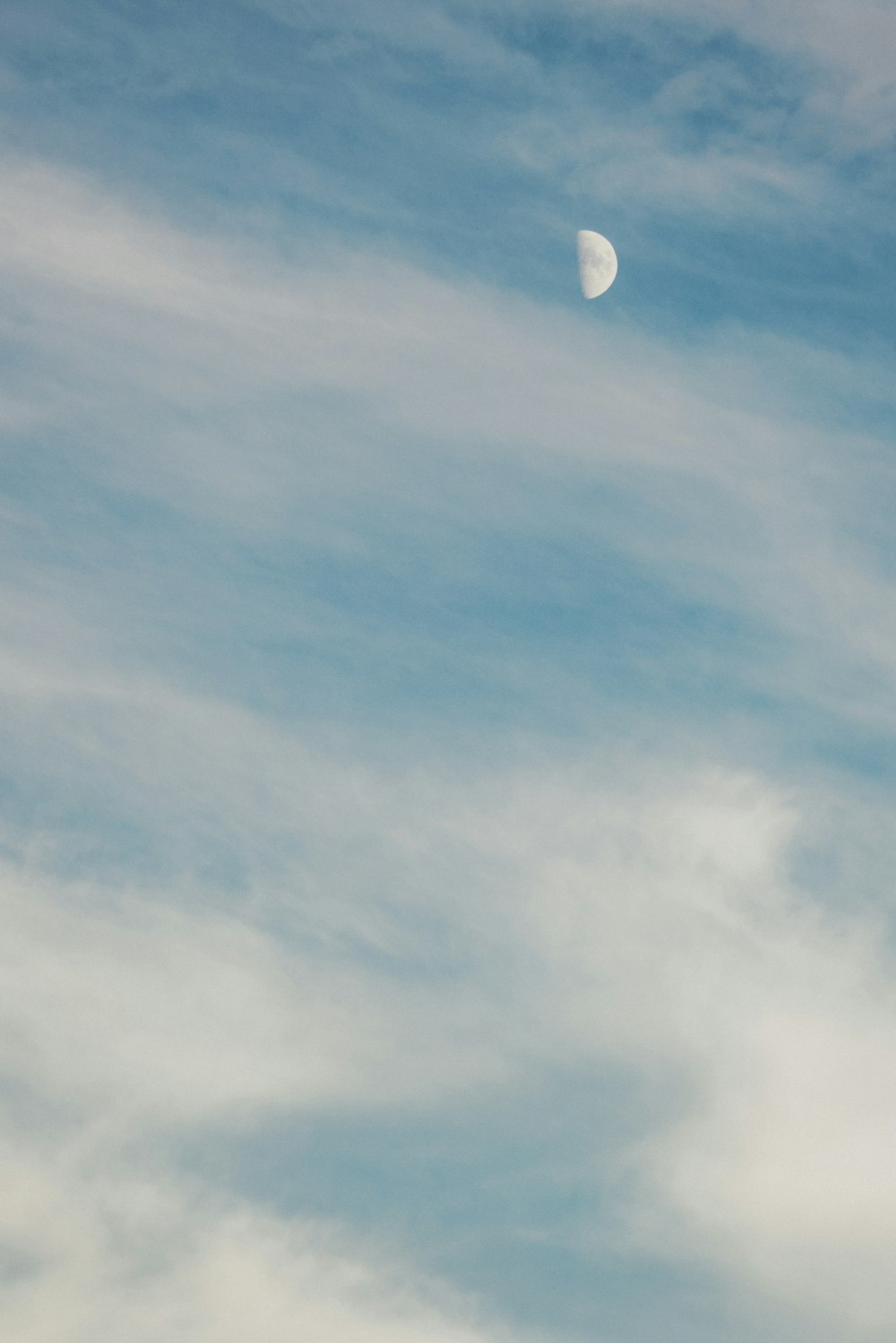 a plane flying in the sky with a half moon in the distance