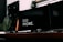 A modern and minimalistic workspace with a dark theme features a keyboard, computer mouse, and dual monitors. The words 'DO MORE' are prominently displayed on one of the screens, suggesting a motivational message.