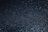 A textured surface with a shimmering effect created by numerous tiny reflective particles spread across a dark background.
