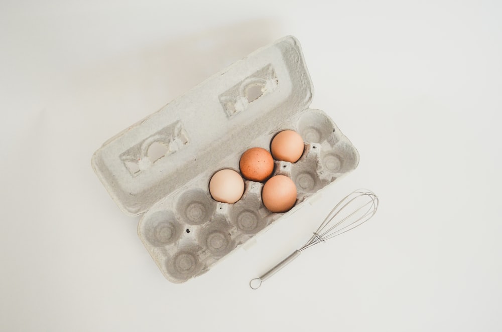 a carton of eggs and a whisk on a table