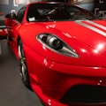 A sleek, red sports car with prominent headlights and silver racing stripes across the hood. The image showcases the car's distinctive aerodynamic design, shiny exterior, and high-performance aspects, with visible details like the wheel and side mirror.