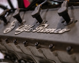 A close-up view of an engine with visible spark plug wires and the Alfa Romeo branding prominently displayed on the engine block.