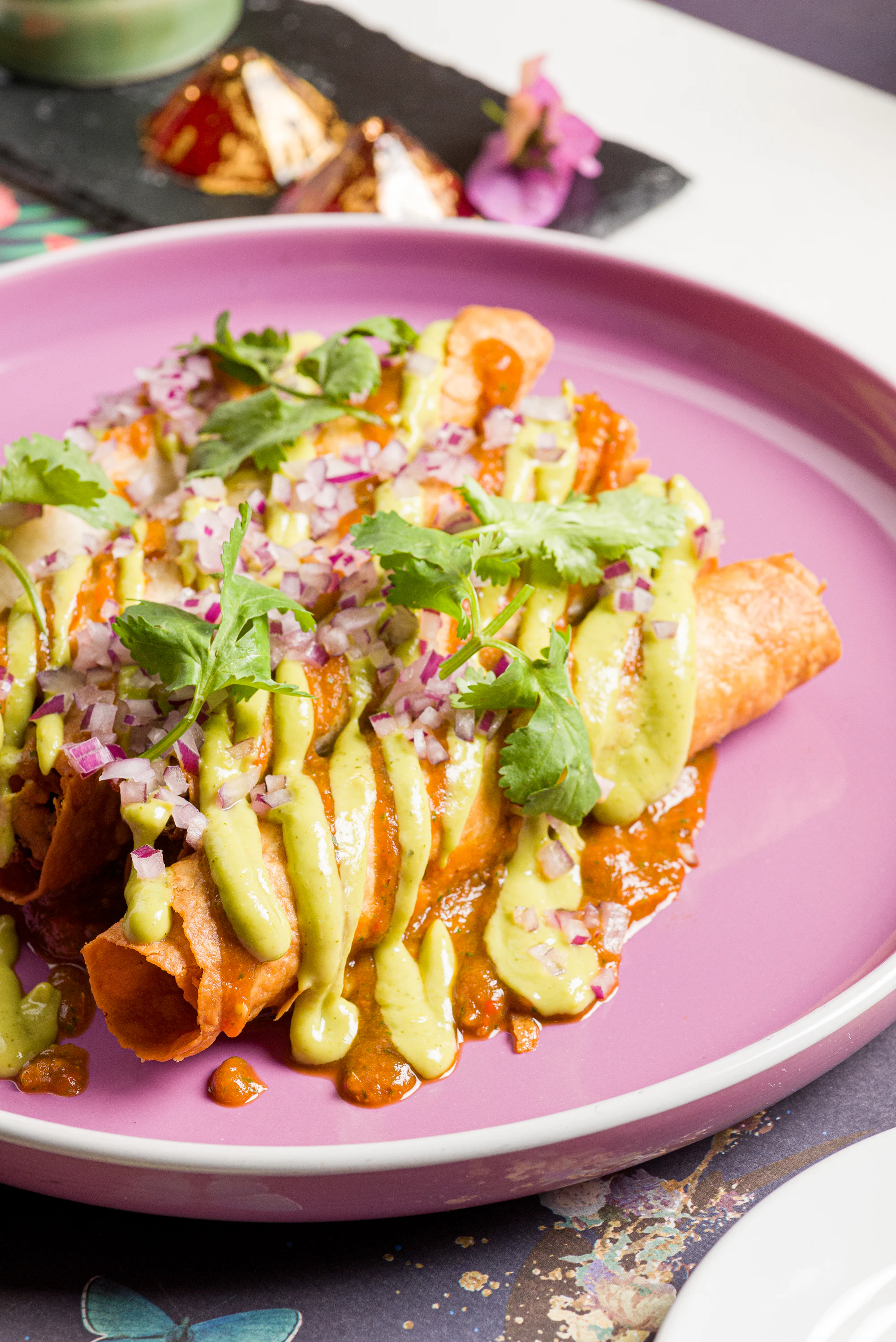 An enchilada plate with red sauce and melted cheese, served on a pink plate
