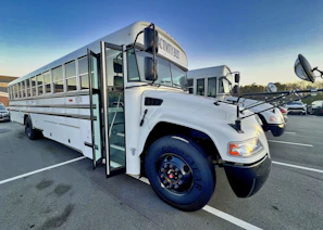 A clean, modern bus parked outside a school building on a sunny day.
