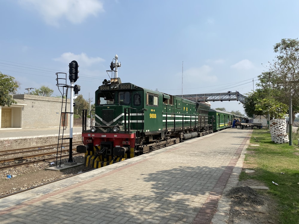 a green train traveling down train tracks next to a lush green field