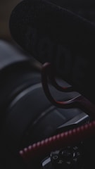 Close-up of a microphone with the brand name partially visible, mounted in front of a camera. The image is dark and moody, with limited lighting highlighting the contours of the equipment.