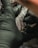 A person wearing black gloves is holding a tattoo machine close to a surface, possibly human skin, with visible tattoo patterns and ink.