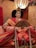 A traditional Japanese doll dressed in an intricate kimono with vibrant colors and detailed embroidery. The doll holds an ornate fan and has a delicate face with a serene expression. A decorative headpiece adorns its hair, and a softly lit, round paper lantern is visible in the background.