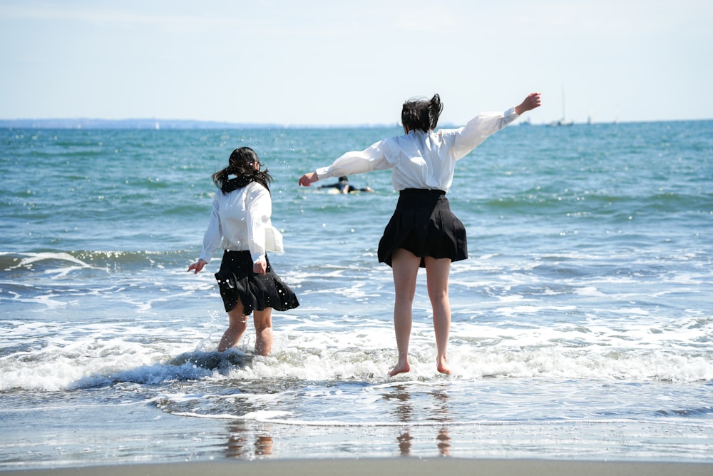 two women standing in the ocean with their arms outstretched