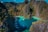 A breathtaking aerial view of a turquoise lagoon surrounded by steep, verdant cliffs. Several traditional boats are floating on the calm water, adding a sense of tranquility and adventure to the scene. The vibrant greenery contrasts sharply with the deep blue and green hues of the water.