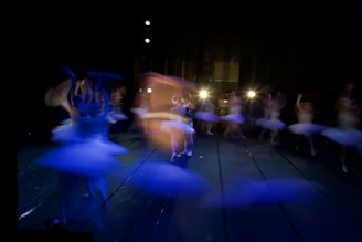 Artistic photo of dancers in motion with soft pink and violet lighting.