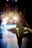 A ballerina in a tutu stands backstage, silhouetted against bright stage lights. Other dancers are visible in the background, preparing for a performance. The scene captures the anticipation and focus of a dance production.
